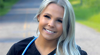 Woman standing on empty path outside in black nurse scrubs smiling at camera
